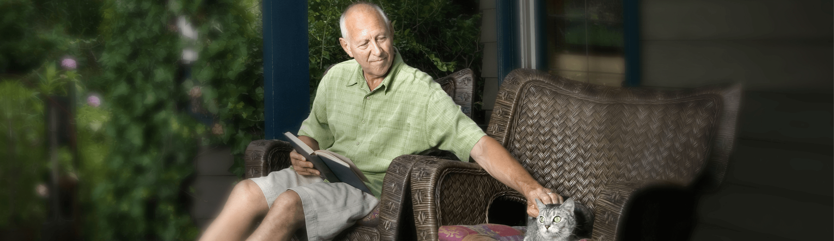 Man with metastatic pancreatic cancer sitting in outdoor chair with a book in his lap and petting a cat