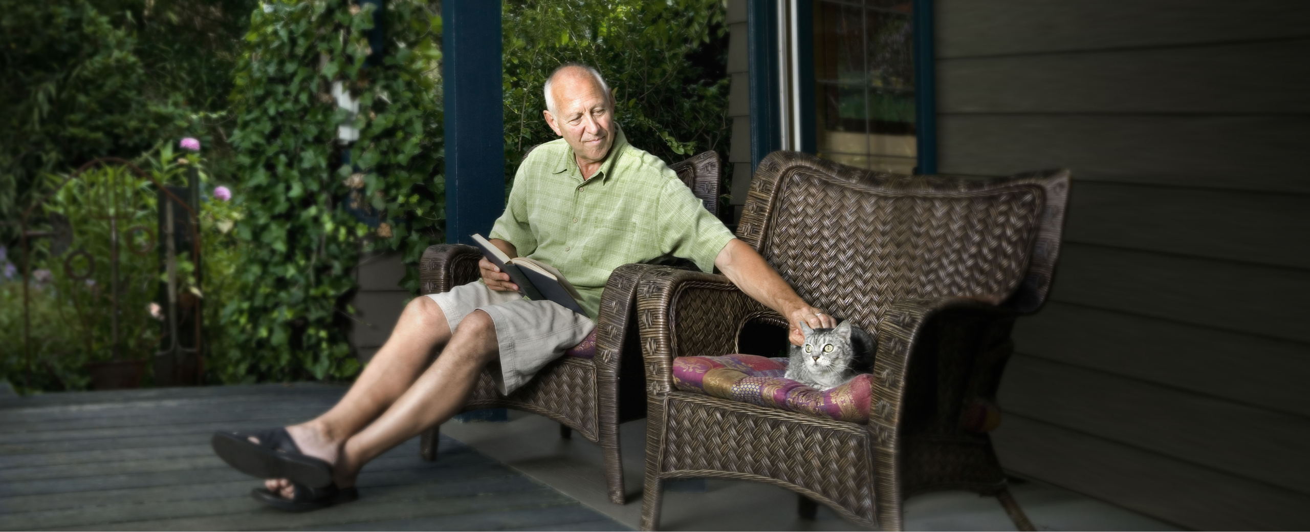 Man with metastatic pancreatic cancer sitting in outdoor chair with a book in his lap and petting a cat.